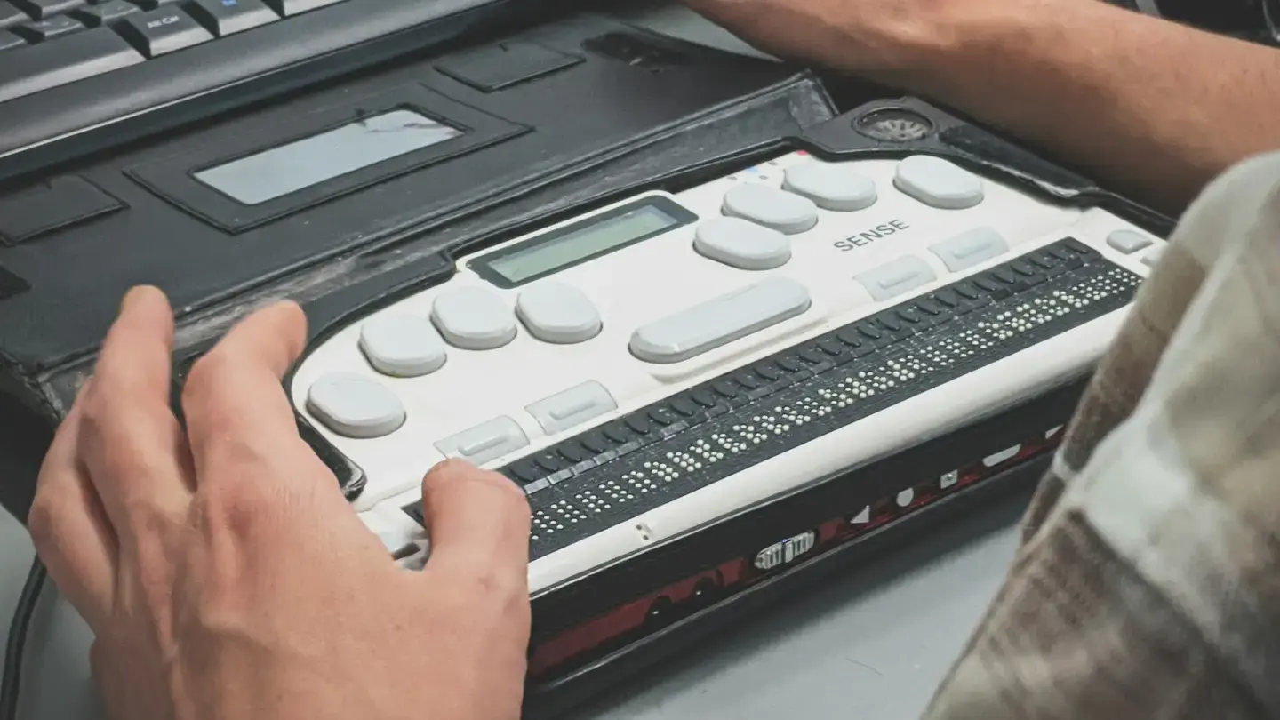 Mains posées sur une plage braille reliée à un clavier d’ordinateur