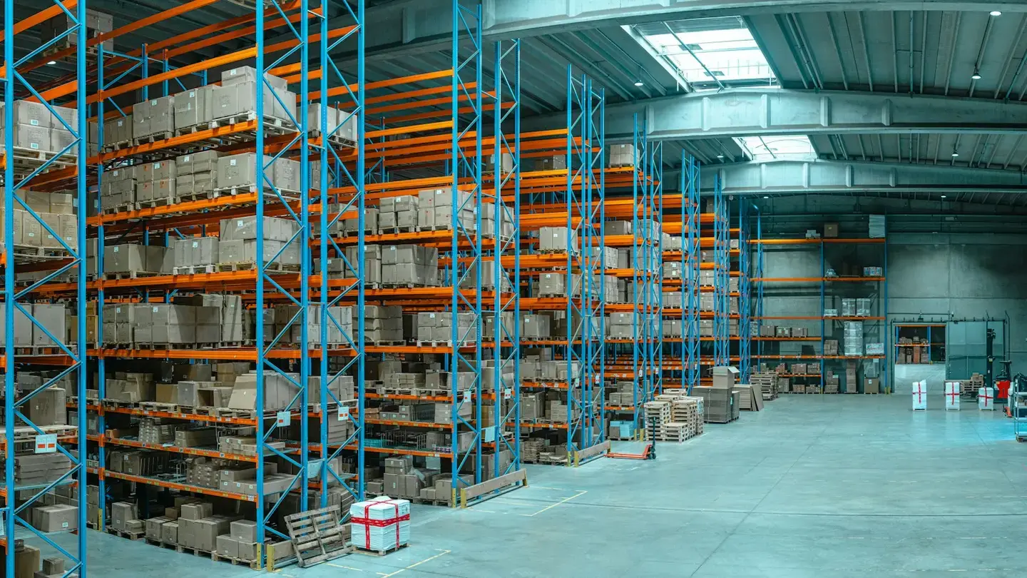 Entrepôt avec de hauts rayonnages bleus et orange chargés de cartons sur palettes