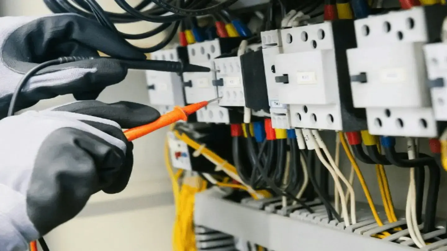 Technicien ganté testant un tableau électrique avec un testeur de tension
