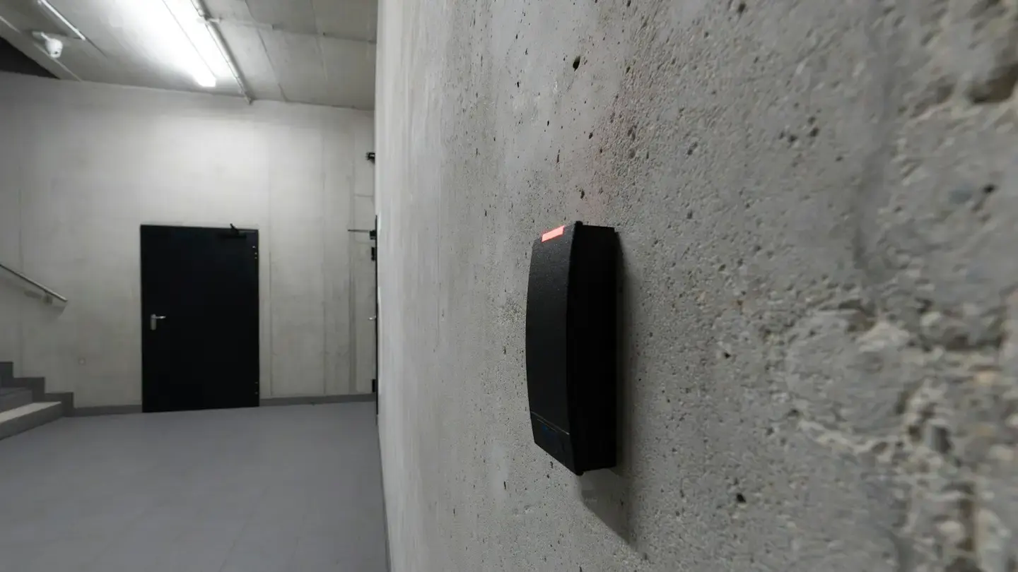 Lecteur de badge fixé sur un mur en béton, à côté d’une porte de service