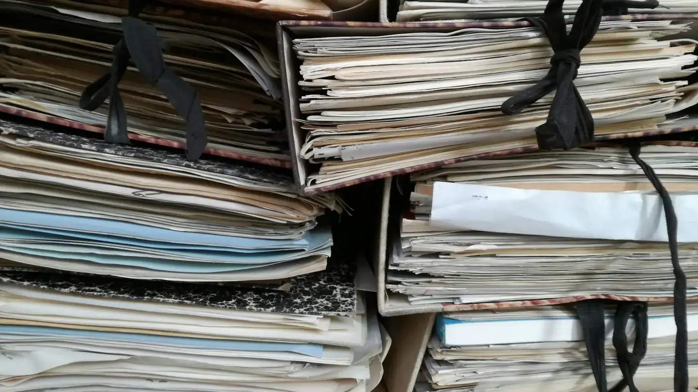 Empilement de chemises cartonnées et de liasses de papiers ficelées, en attente de traitement