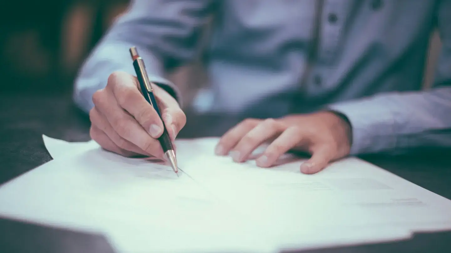 Main tenant un stylo au-dessus d’un document posé sur un bureau, prête à signer