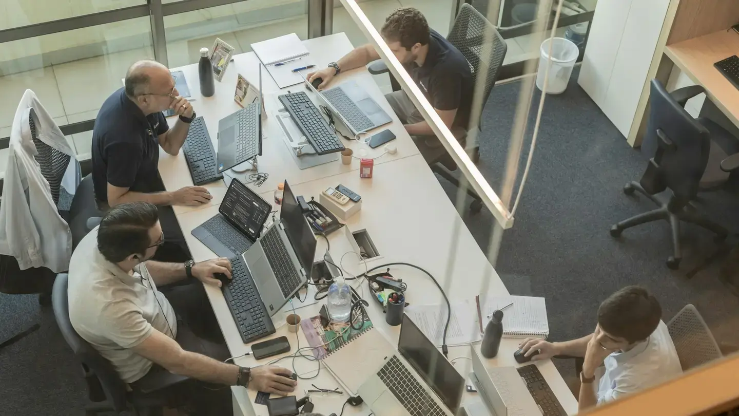 Vue en plongée d’une équipe travaillant sur des ordinateurs portables dans un bureau vitré