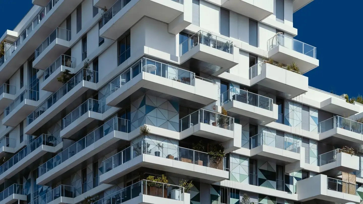 Façade d’un immeuble résidentiel blanc aux balcons en verre sous un ciel bleu