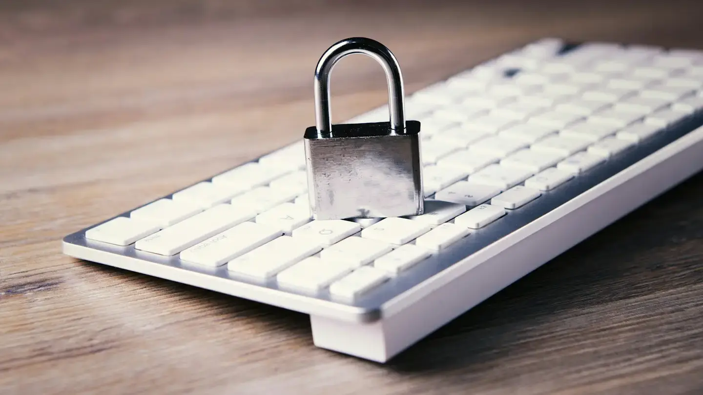 Cadenas métallique posé sur un clavier d’ordinateur blanc, sur un bureau en bois