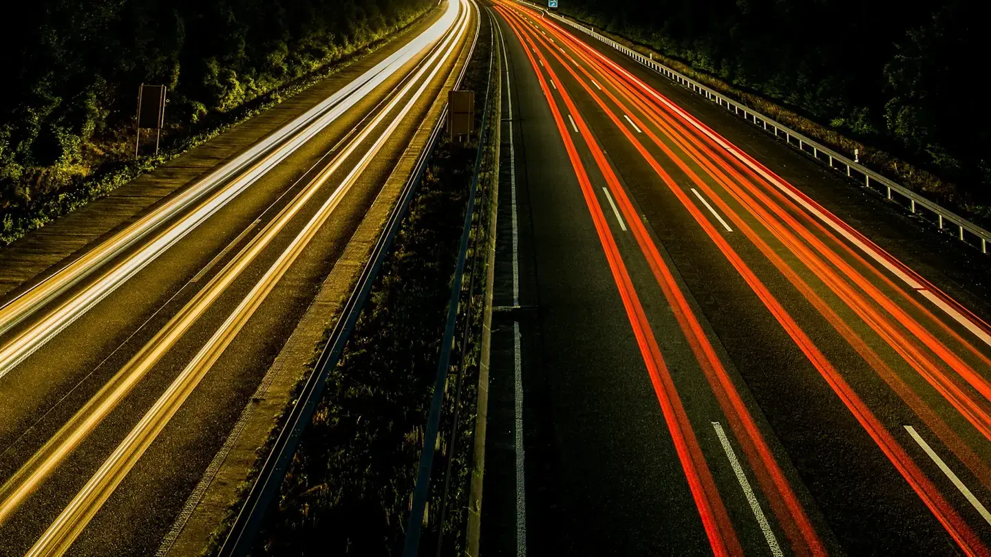 Autoroute de nuit photographiée en pose longue, traînées lumineuses des véhicules