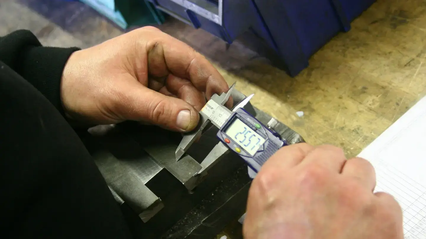Mains d’un technicien mesurant une pièce métallique avec un pied à coulisse numérique