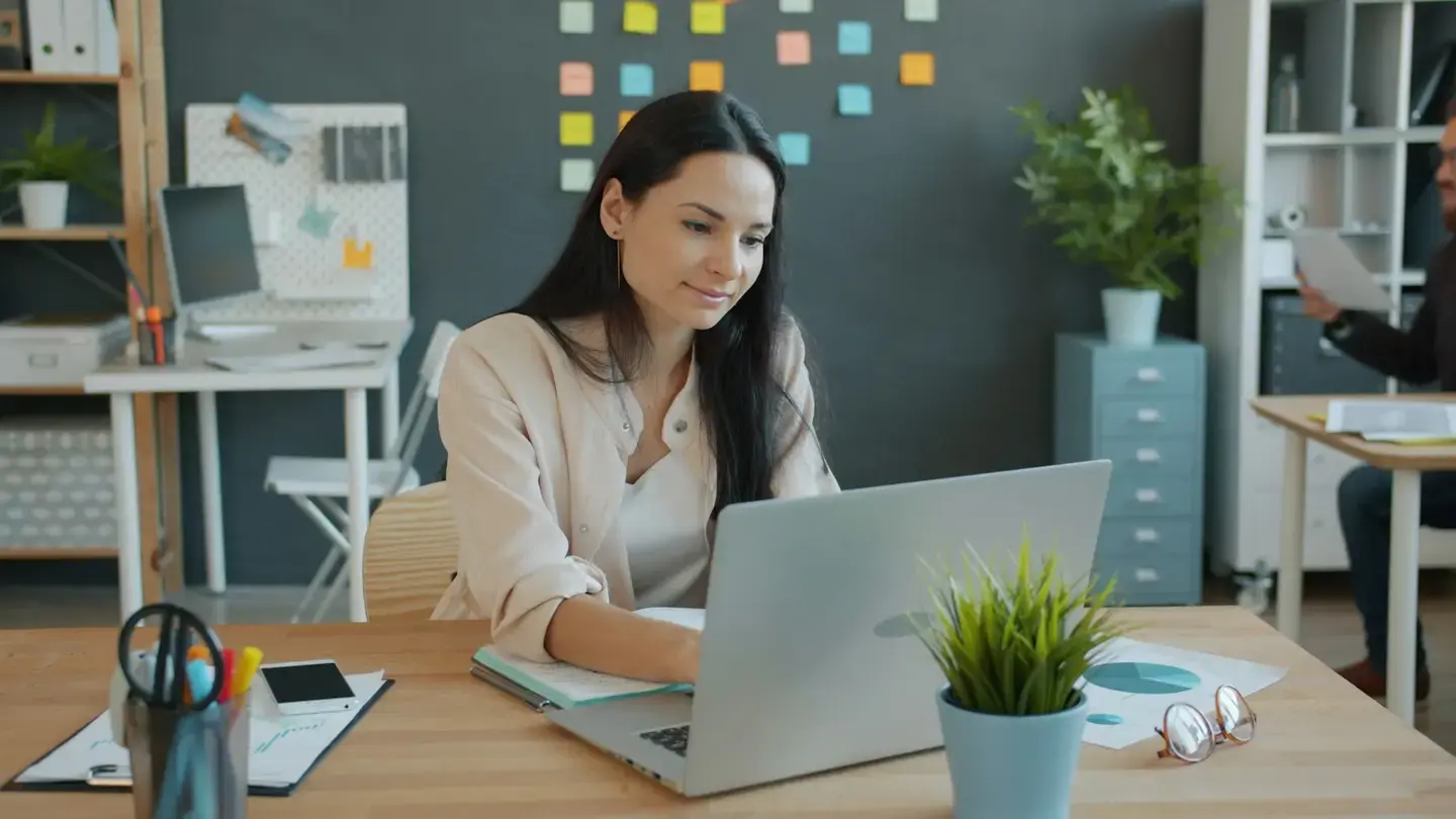 Collaboratrice travaillant sur un ordinateur portable dans un bureau, notes adhésives au mur