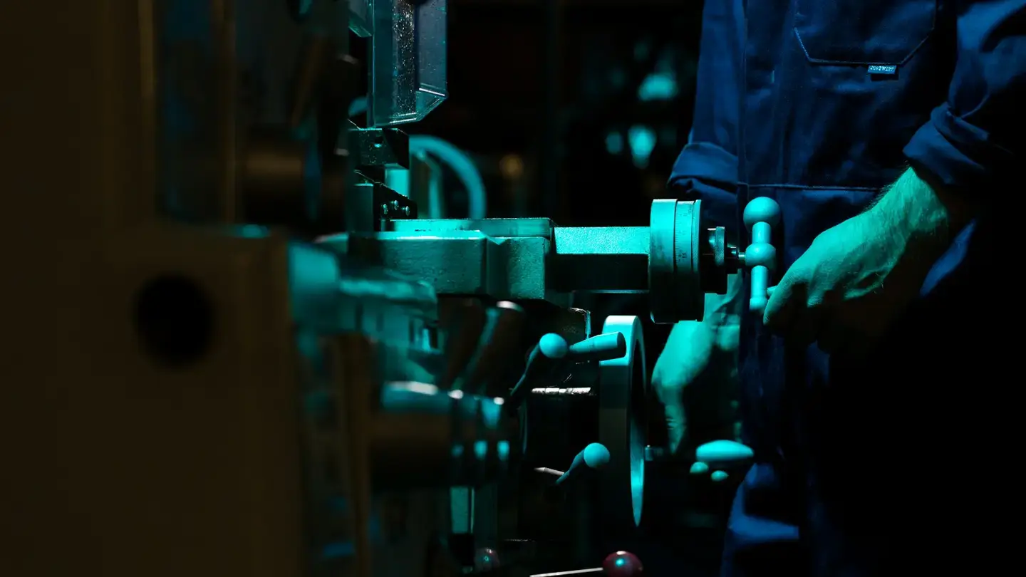 Opérateur en bleu de travail manœuvrant les volants d’une machine-outil dans un atelier sombre