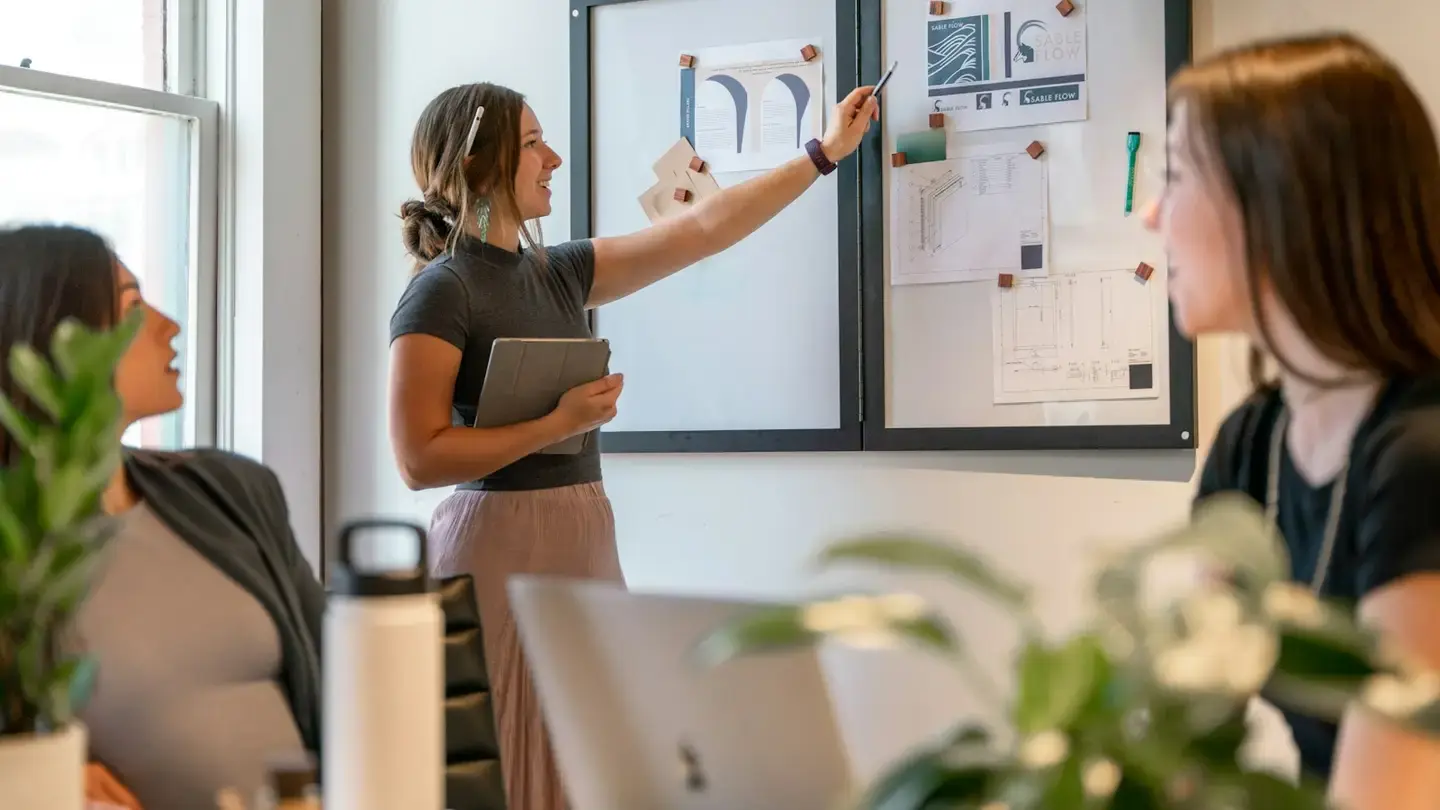 Petite équipe réunie autour d’une table, une participante désigne des schémas affichés au mur