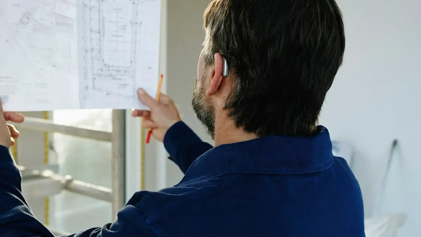 Un conducteur de travaux de dos consulte un plan papier sur un chantier en cours