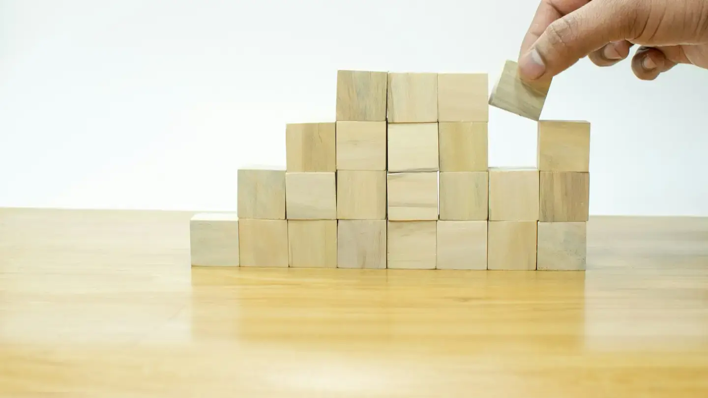 Main posant un cube de bois au sommet d’un assemblage de blocs sur une table