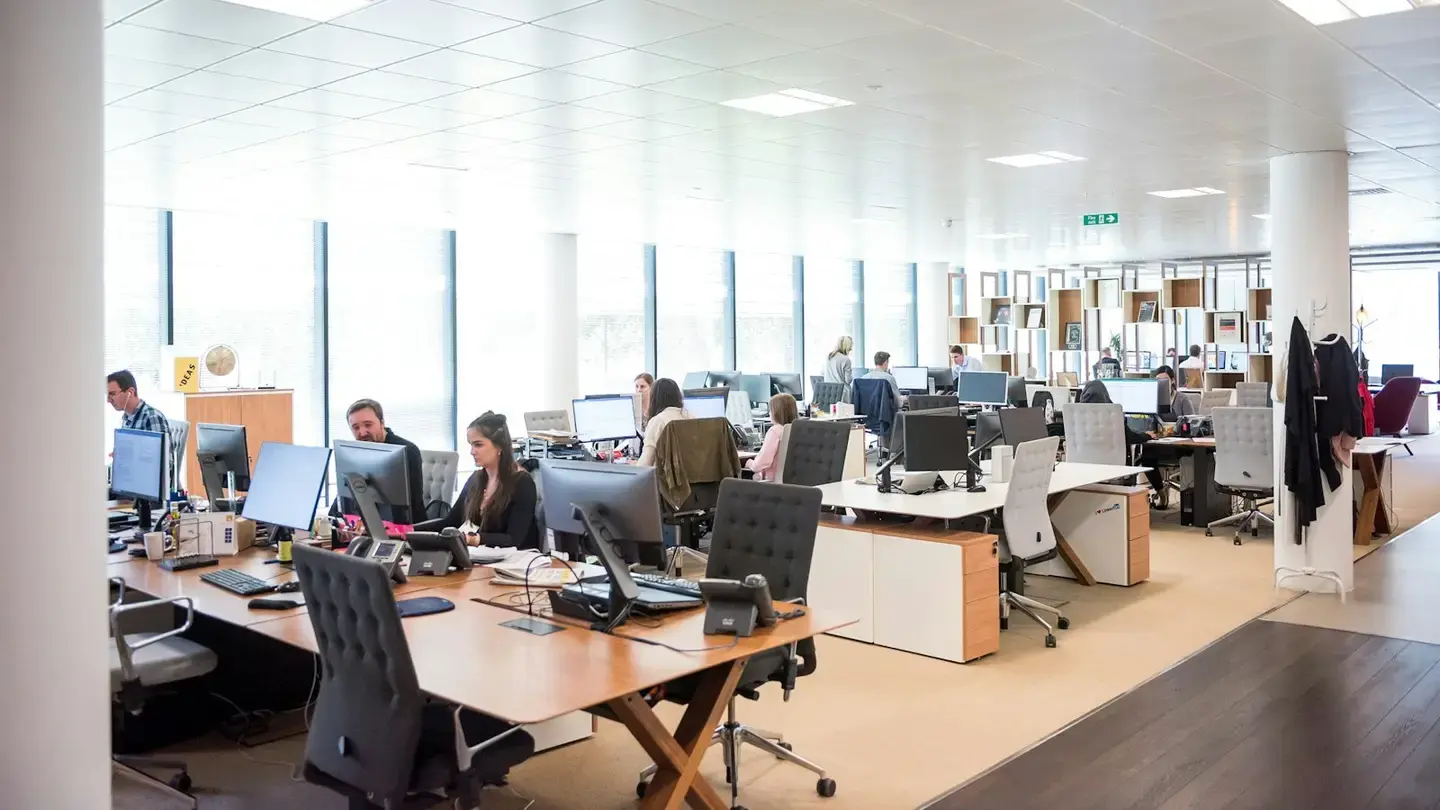 Plateau de bureaux ouvert où des équipes travaillent sur des postes informatiques