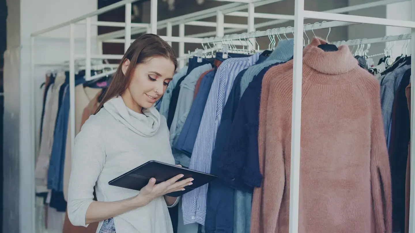 Une commerçante consulte une tablette entre des portants de vêtements dans sa boutique