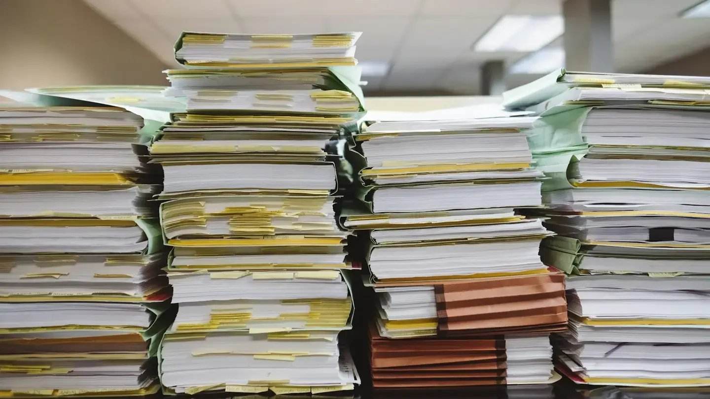 Piles de dossiers papier et de classeurs annotés de marque-pages jaunes dans un bureau