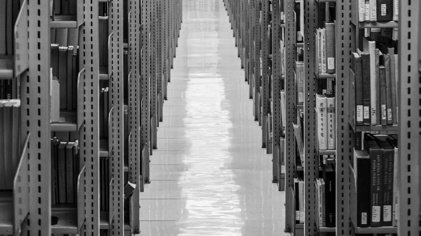 Allée centrale entre de longues rangées de rayonnages d’archives, en noir et blanc