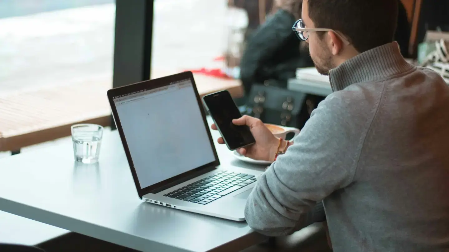 Homme consultant son smartphone devant un ordinateur portable ouvert sur une table