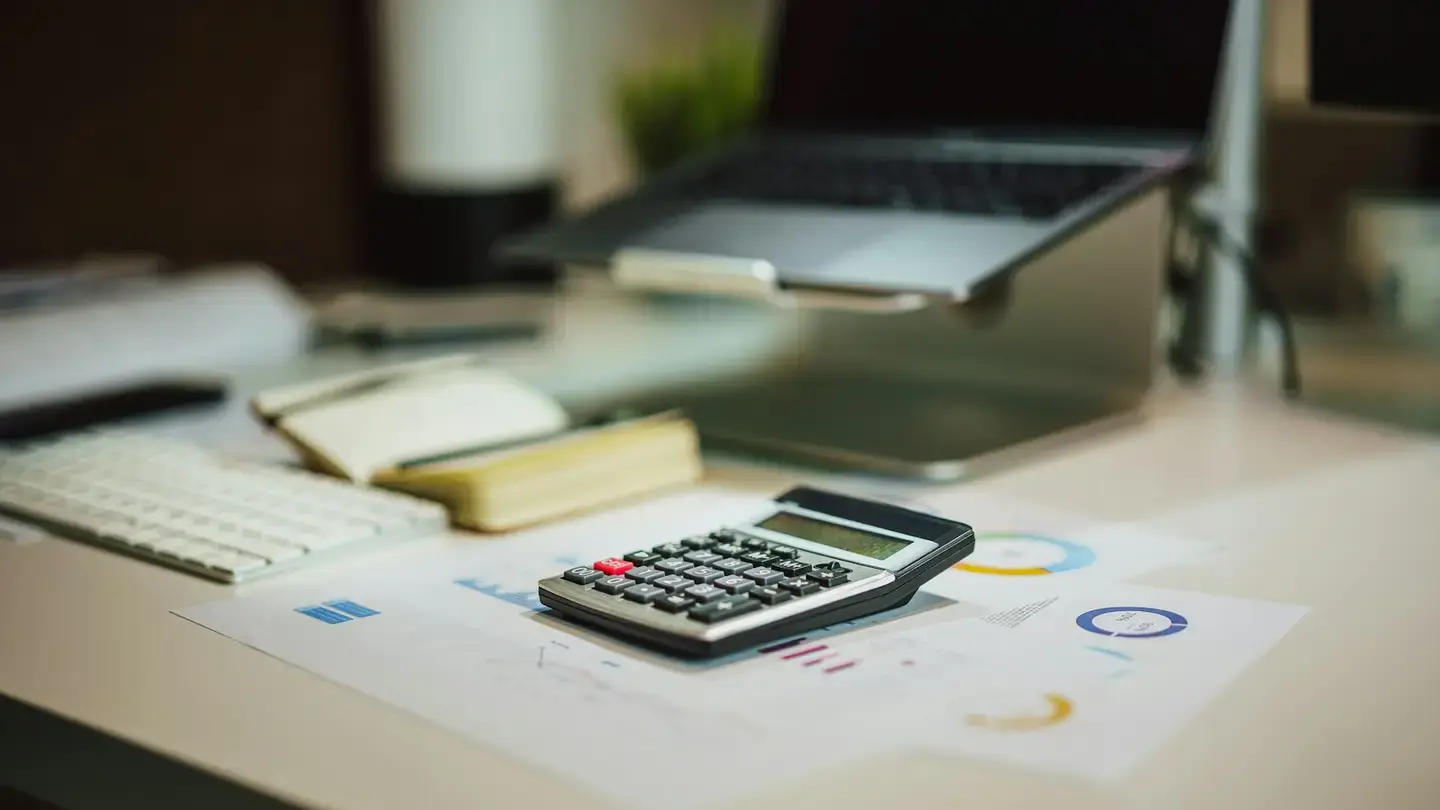 Calculatrice posée sur des documents financiers avec graphiques, devant un ordinateur portable