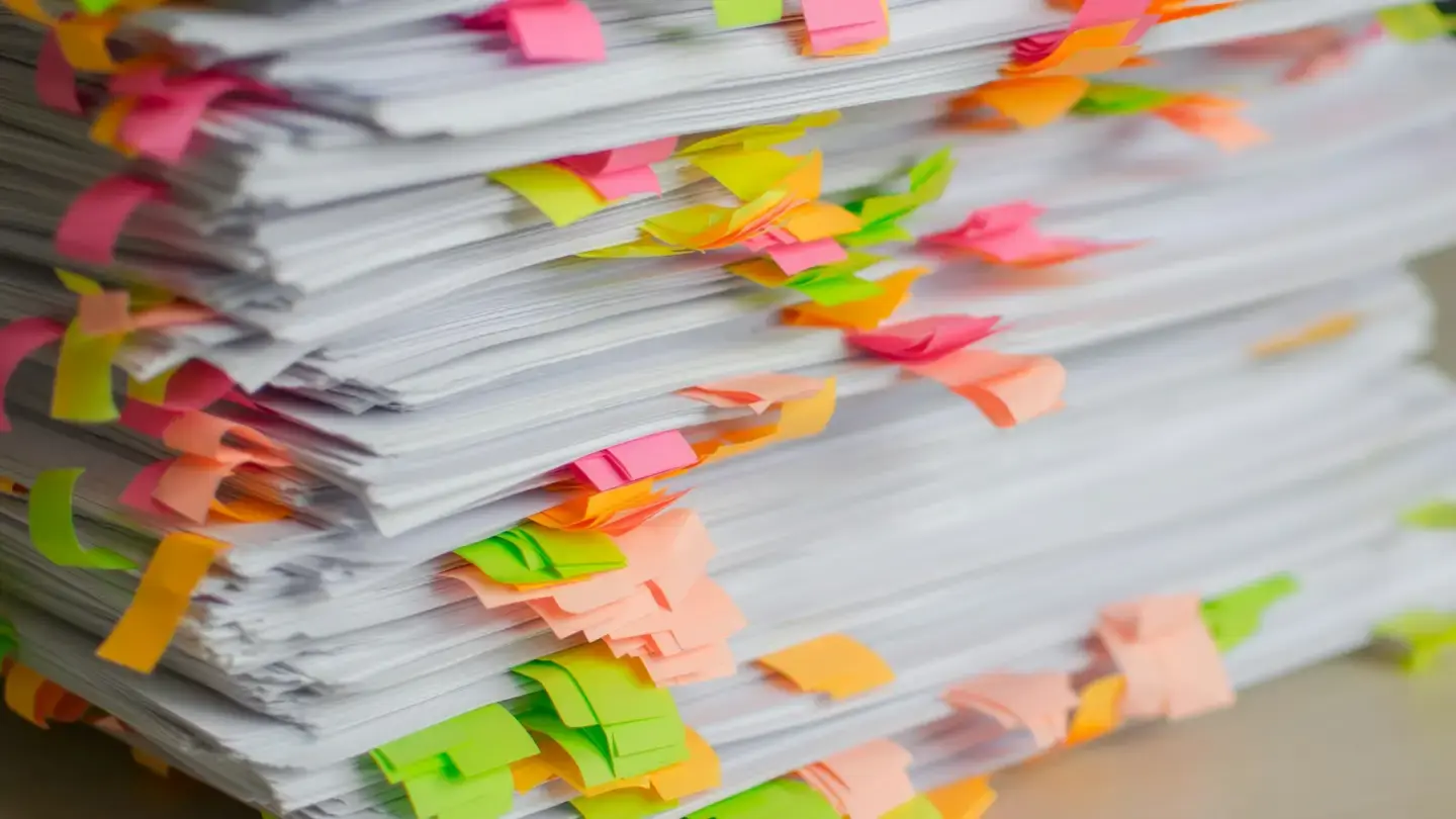 Pile de dossiers papier hérissée de marque-pages adhésifs de couleur