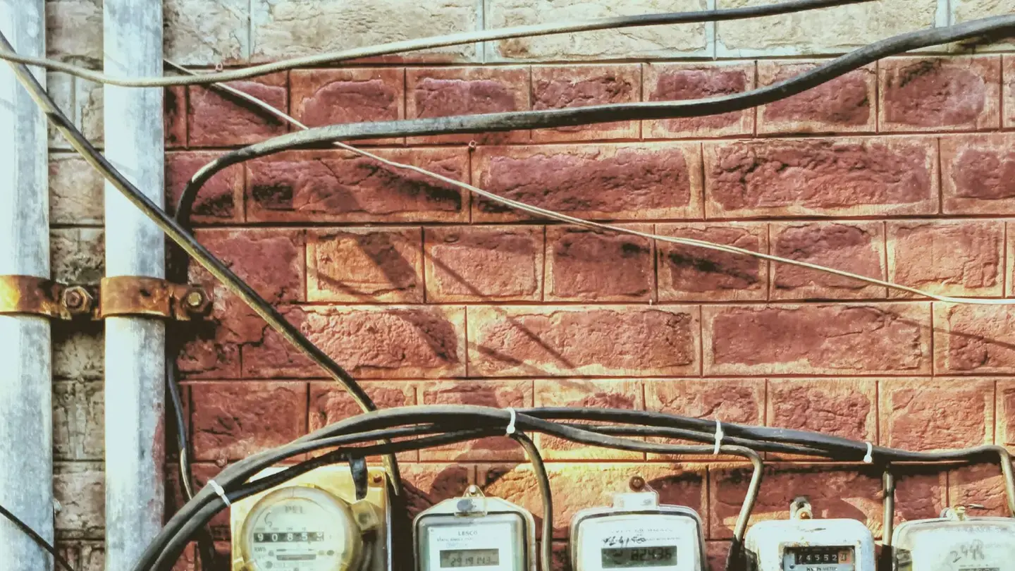 Rangée de compteurs électriques sous un enchevêtrement de câbles sur un mur de briques