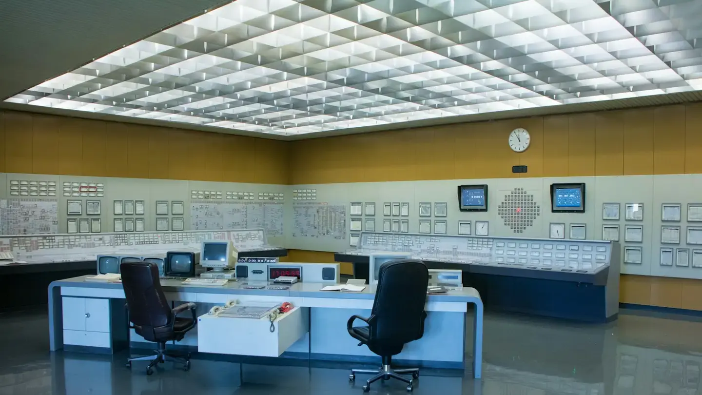 Salle de contrôle avec pupitres, écrans de supervision et horloge murale