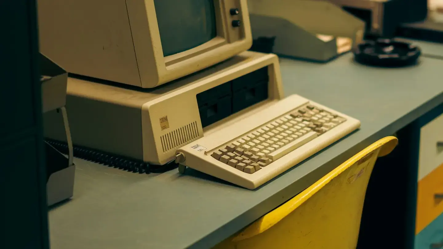 Ancien ordinateur beige avec son écran cathodique et son clavier posé sur un bureau gris