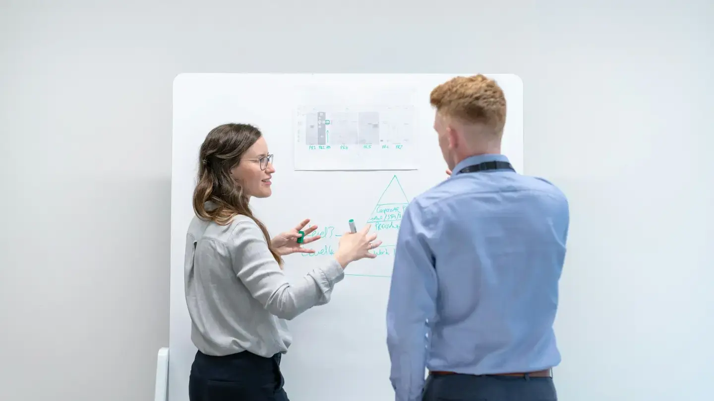 Deux collègues échangent devant un tableau blanc où sont affichés des graphiques et un schéma