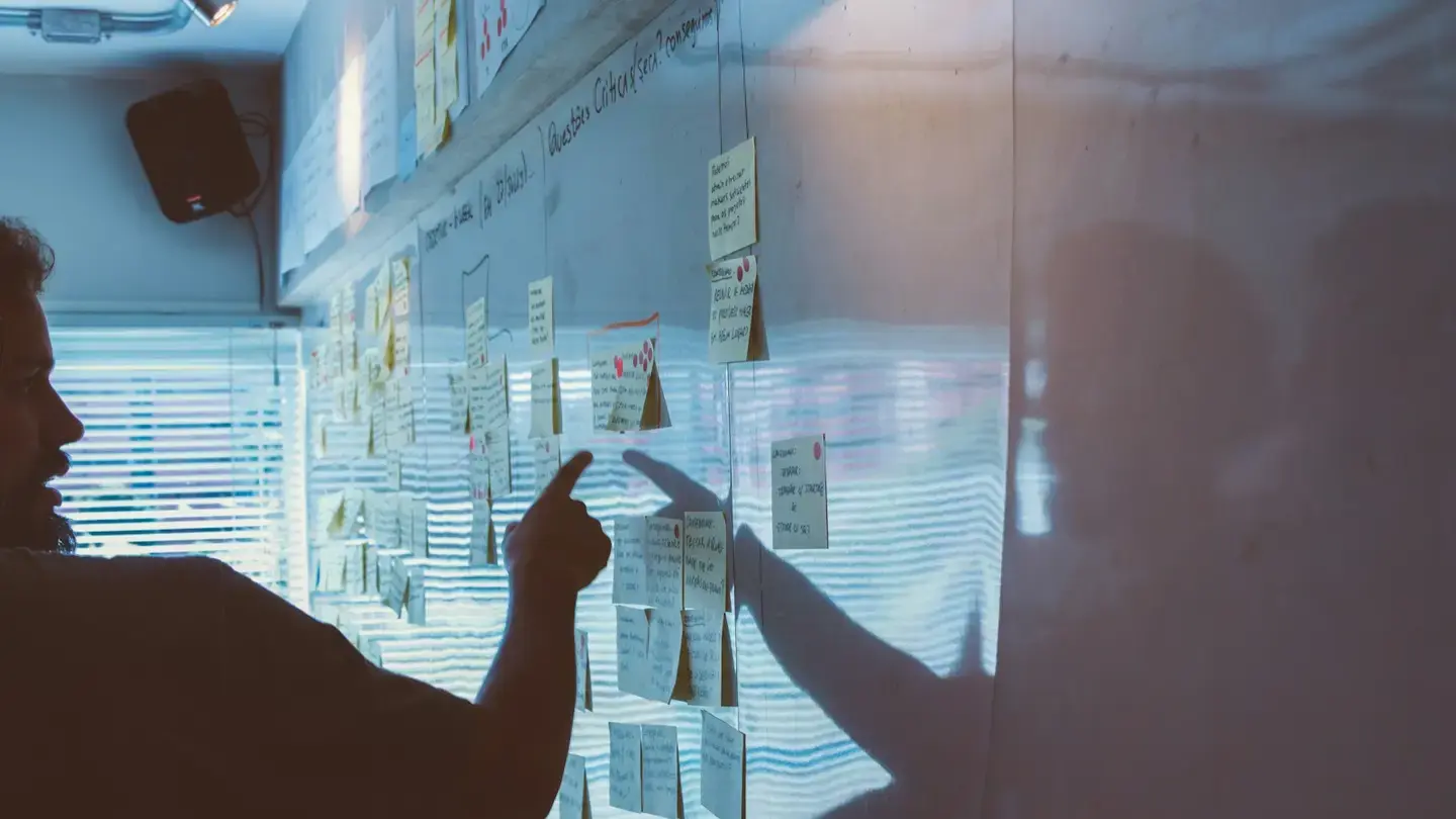 Un homme désigne une note adhésive sur un mur couvert de notes organisées en colonnes