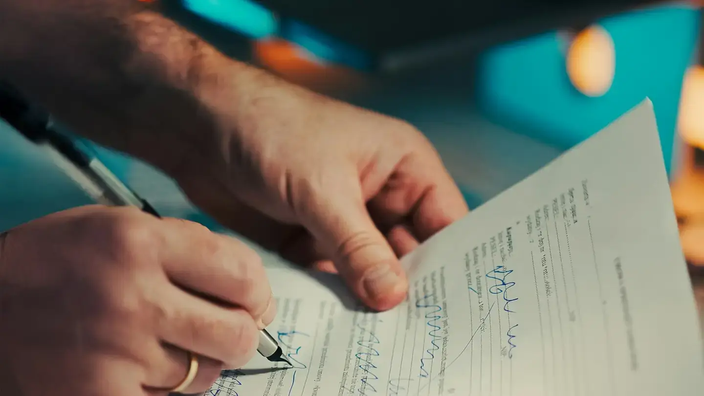 Mains annotant au stylo un document contractuel imprimé, page par page
