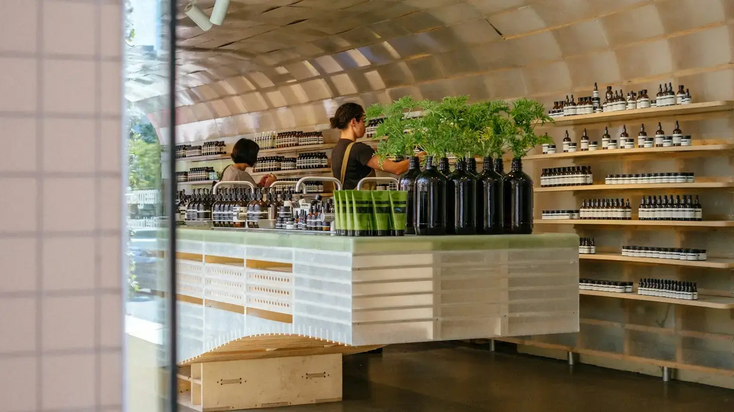 Intérieur d’une boutique aux étagères de flacons, deux vendeuses mettent en place le comptoir