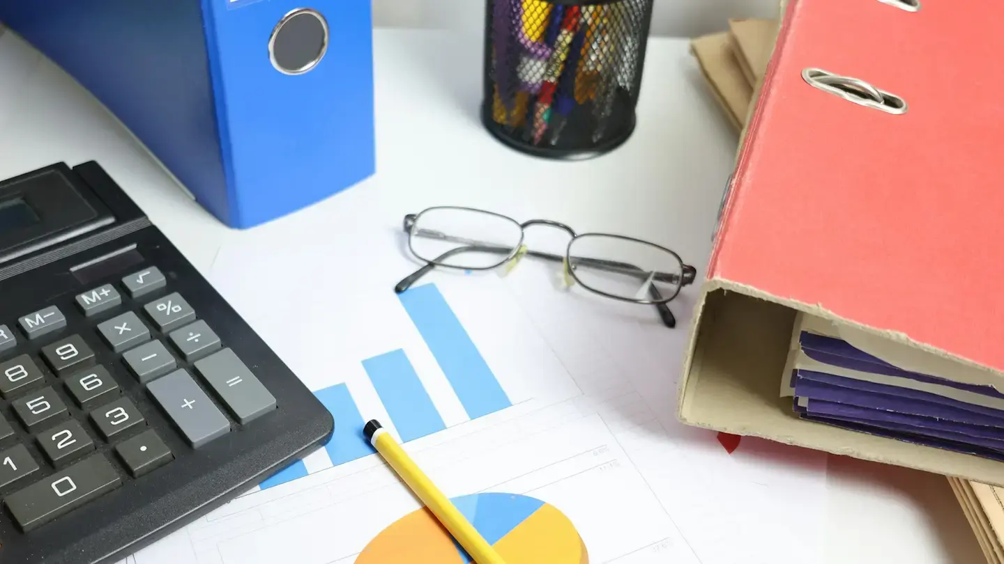 Bureau avec calculatrice, classeurs colorés, lunettes et graphiques en barres imprimés