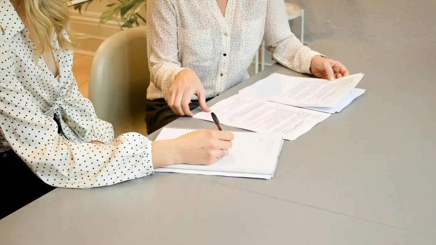 Deux personnes relisent et annotent des documents de mission sur une table de réunion