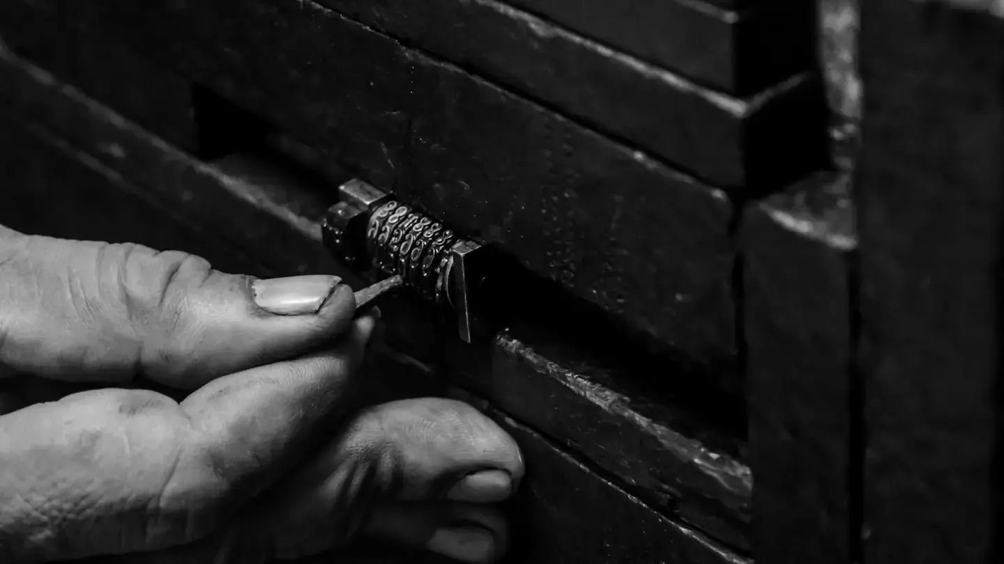 Main manipulant un cadenas à code sur un coffre en bois, en noir et blanc