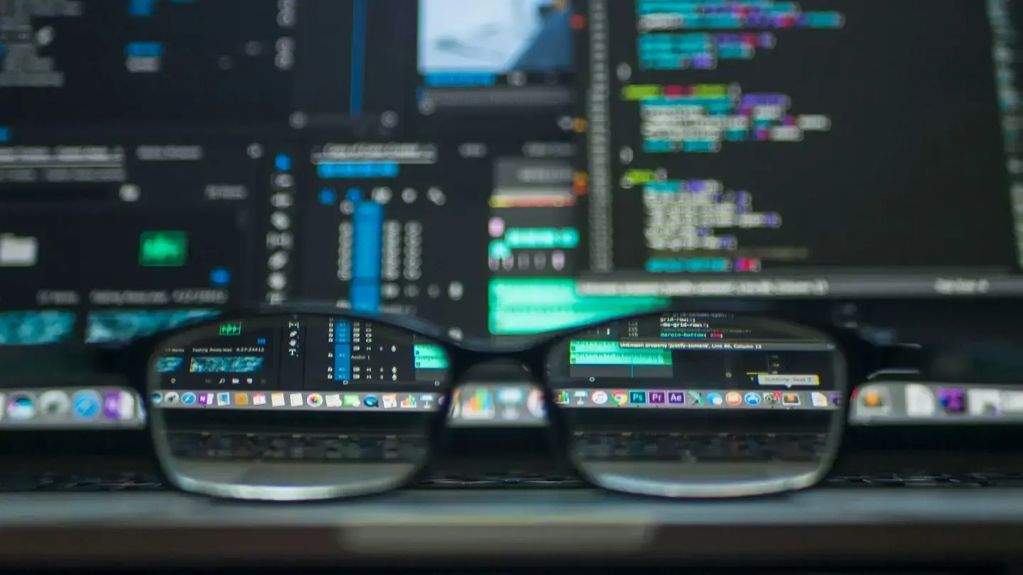 Lunettes posées devant un écran affichant des lignes de code colorées, floues à l’arrière-plan