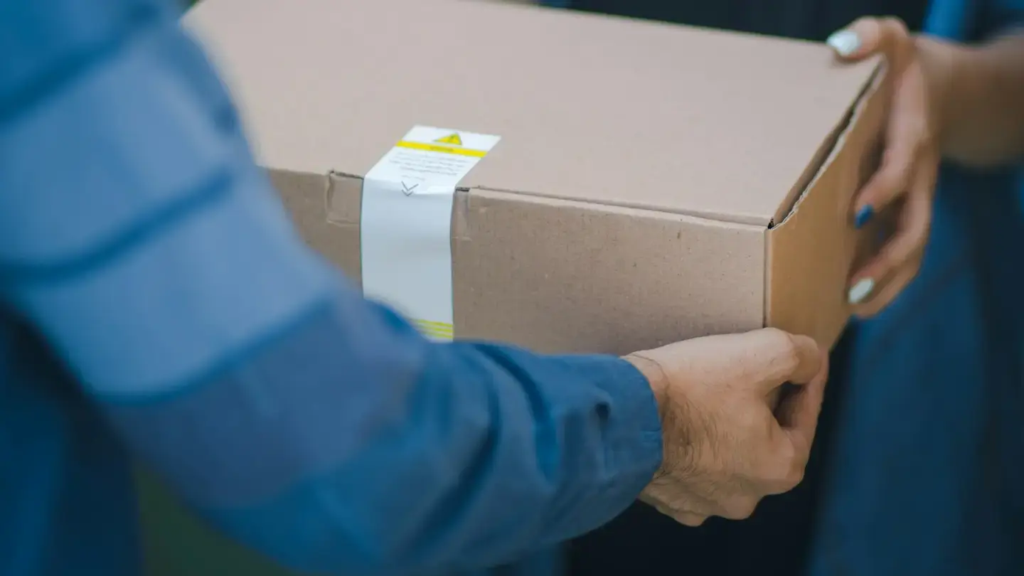 Un livreur remet un carton à son destinataire, gros plan sur les mains et le colis