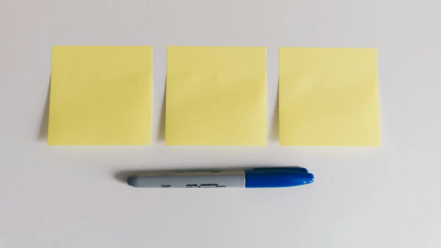 Trois notes adhésives vierges et un feutre posés sur une table blanche