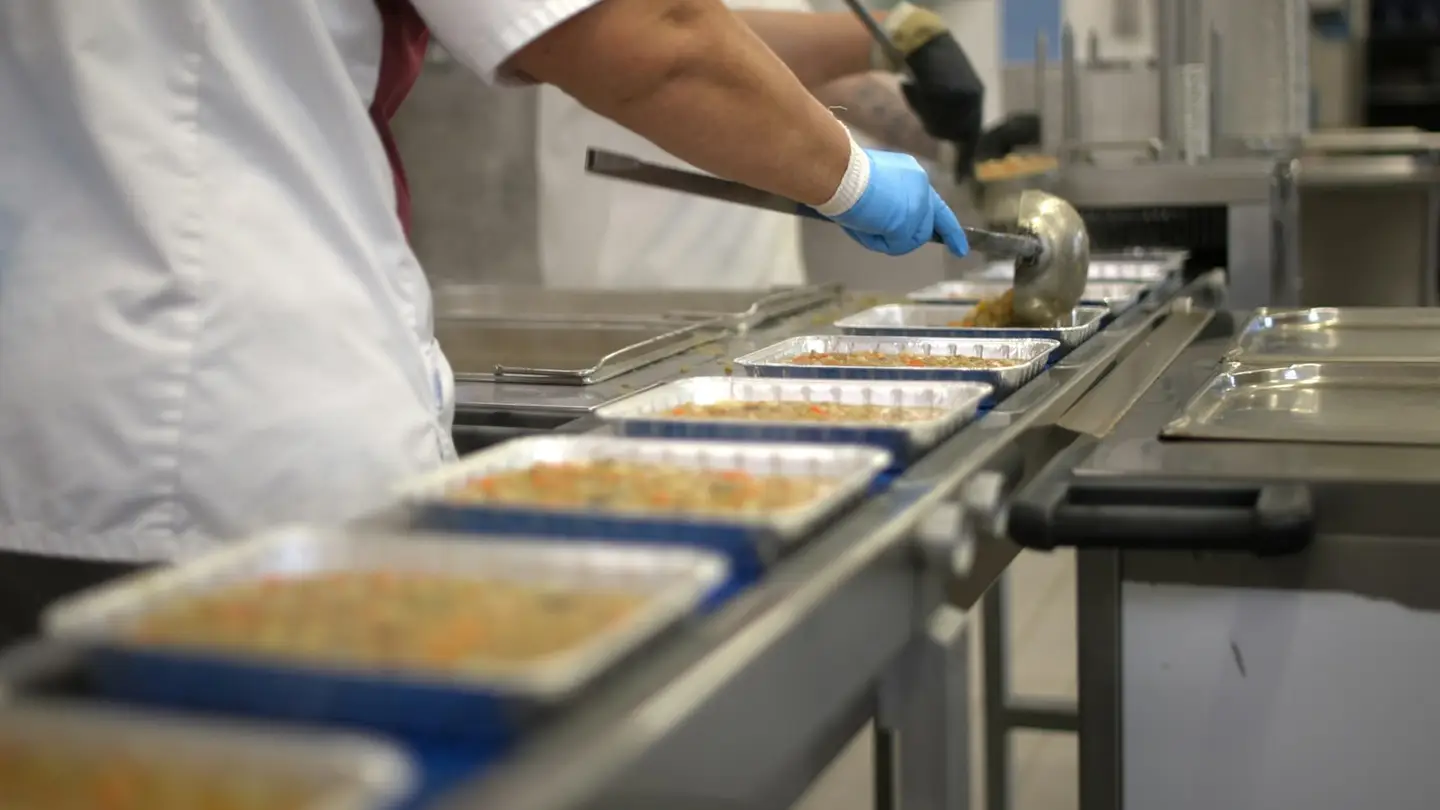 Une opératrice remplit des barquettes de plats cuisinés sur une ligne de conditionnement