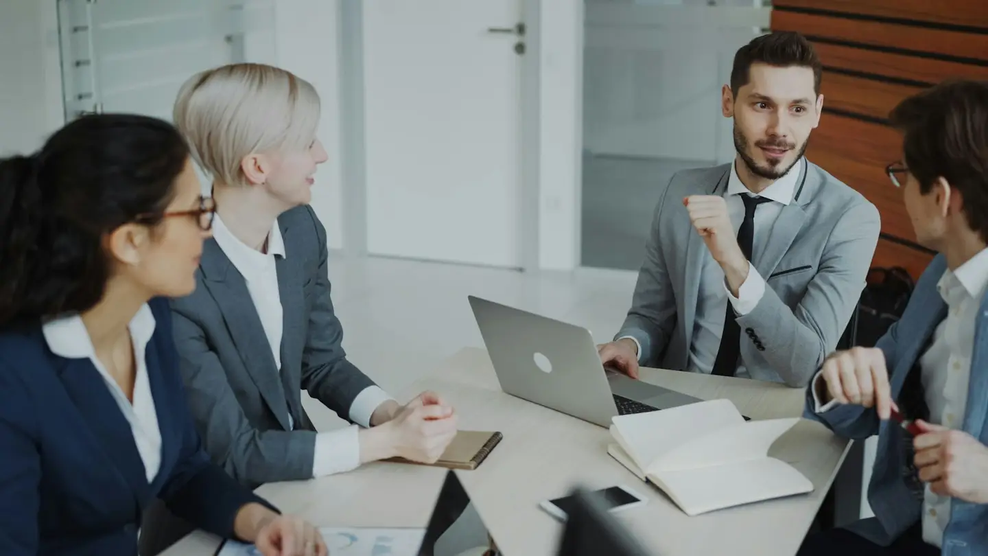 Une équipe de direction discute autour d’une table de réunion avec un ordinateur portable