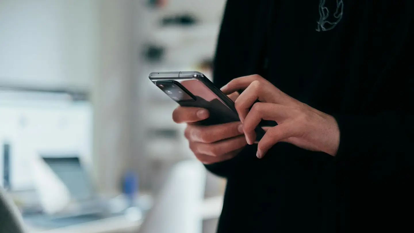 Une personne utilise son smartphone dans un bureau, un ordinateur portable en arrière-plan
