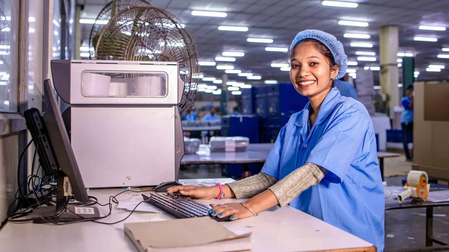 Opératrice souriante assise devant un poste informatique dans un atelier de production