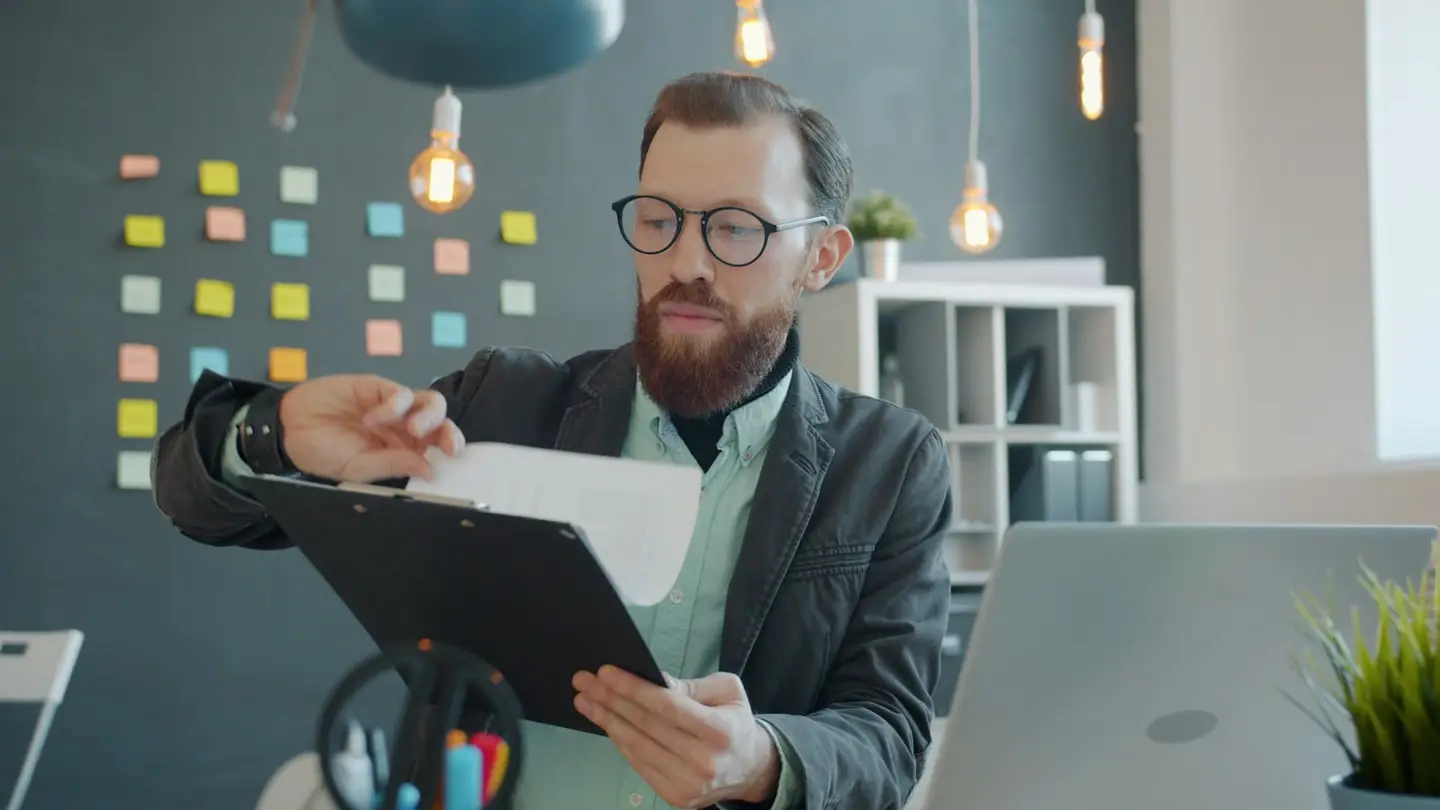 Un collaborateur consulte un formulaire papier sur un porte-documents, ordinateur portable ouvert à côté