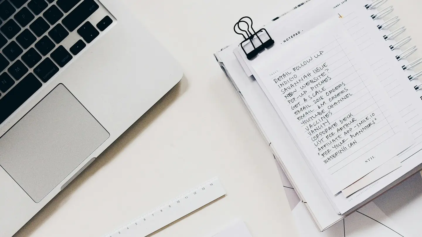 Ordinateur portable ouvert à côté d’un bloc-notes couvert d’une liste manuscrite