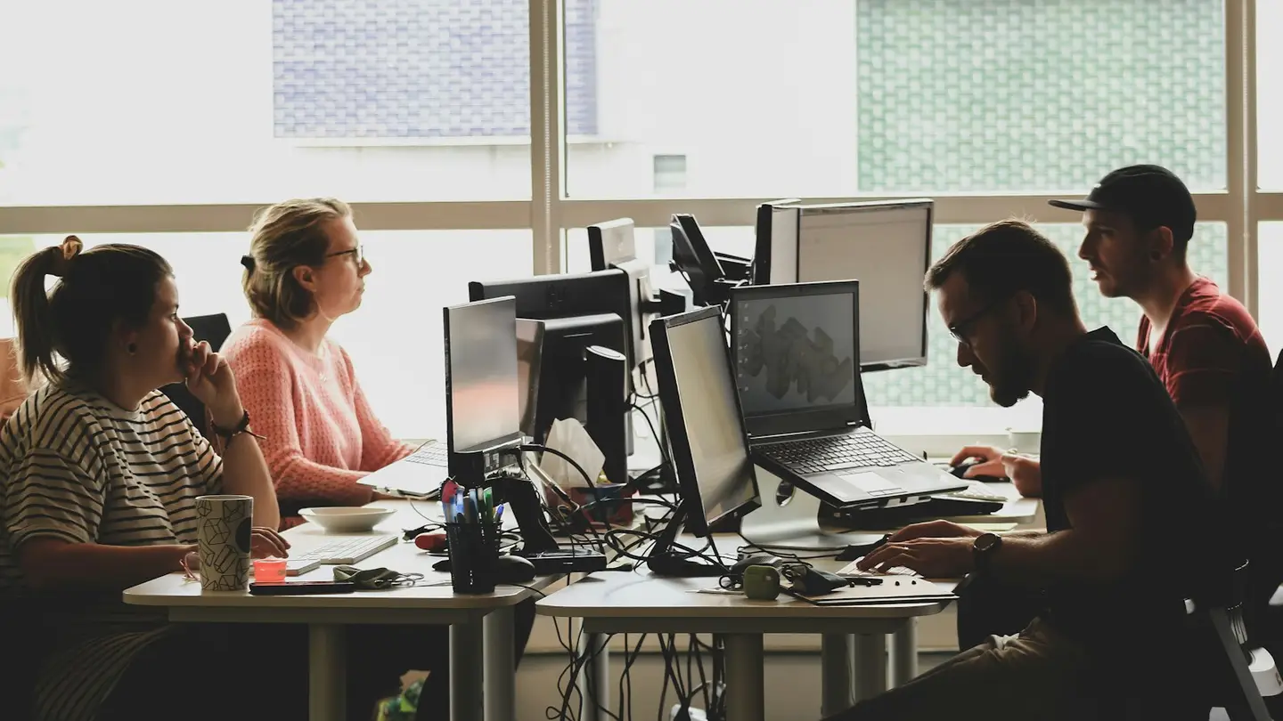 Une équipe de développeurs travaille sur plusieurs écrans dans un bureau baigné de lumière