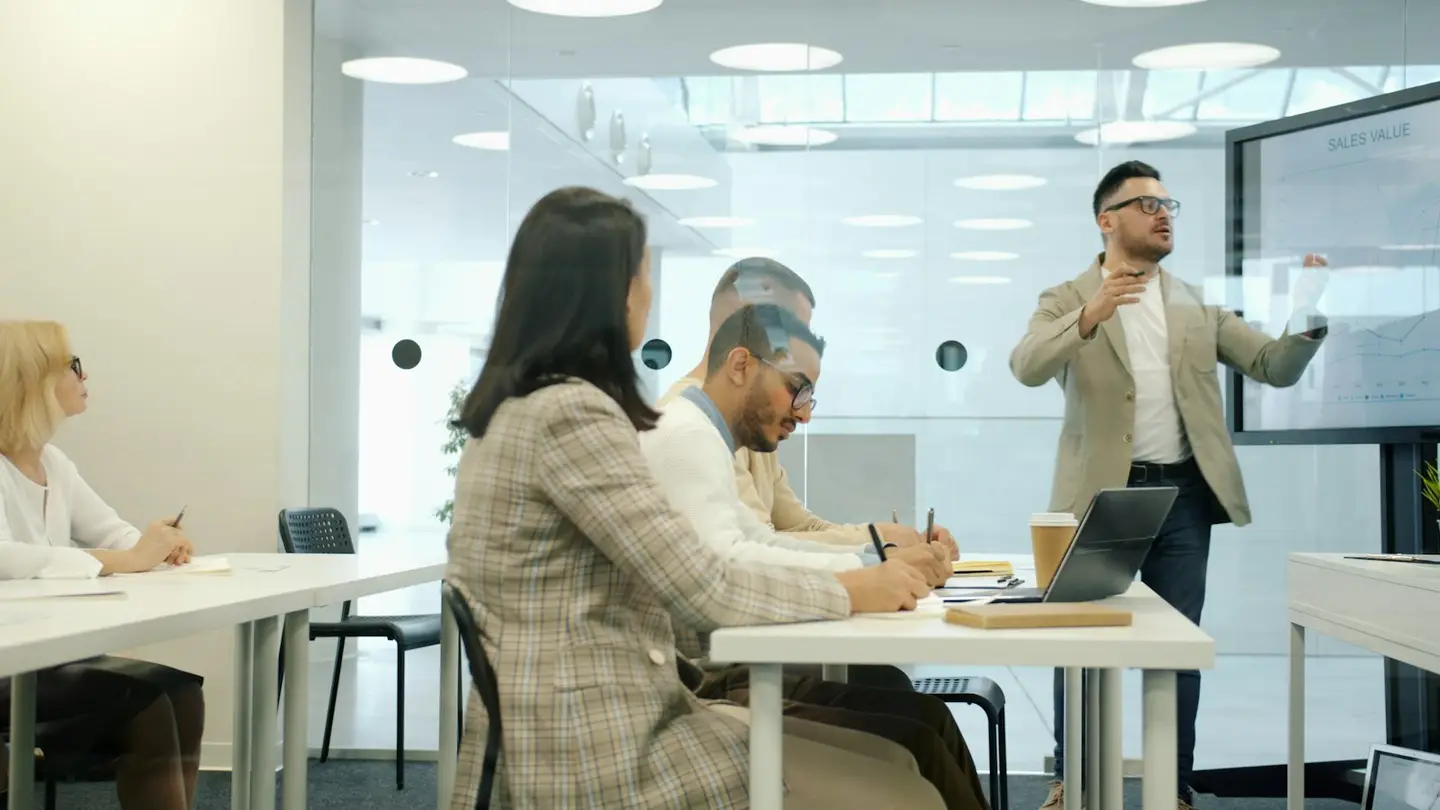 Un intervenant présente des graphiques sur un écran à des collègues qui prennent des notes