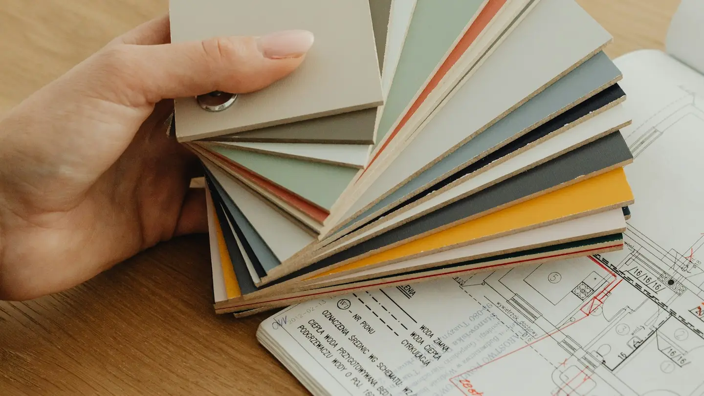 Main tenant un nuancier d’échantillons de finitions au-dessus de plans techniques