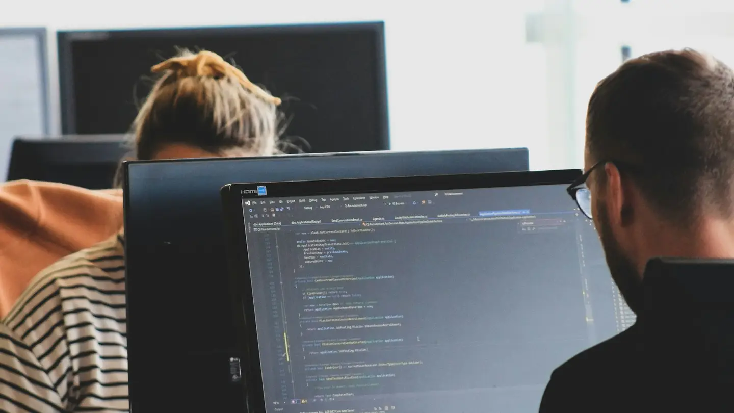 Deux développeurs travaillant sur des écrans affichant du code dans un bureau lumineux
