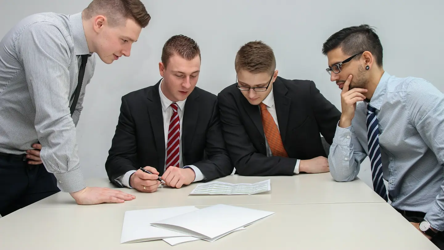 Quatre collaborateurs penchés sur des documents posés sur une table de réunion