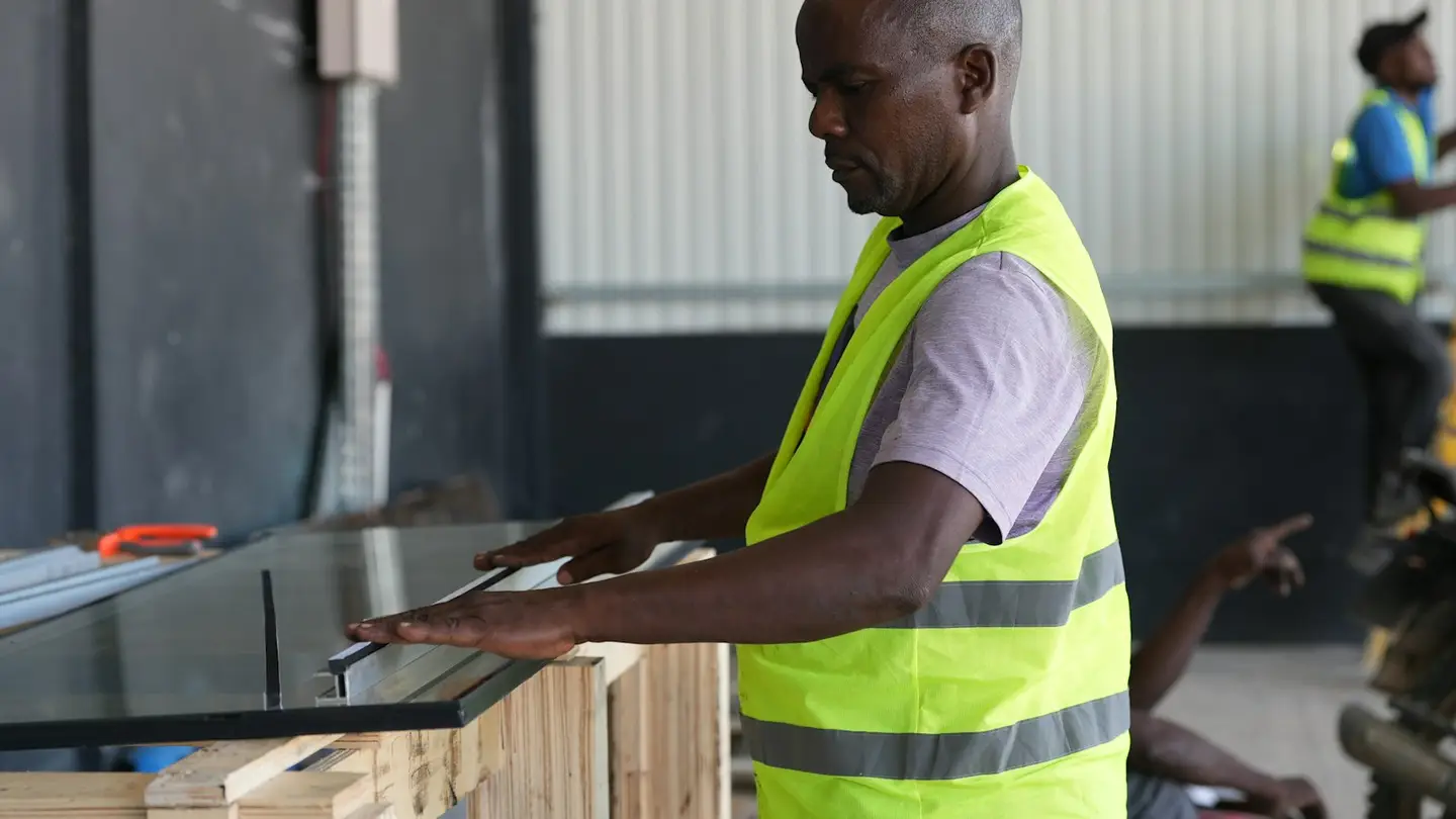 Un artisan en gilet de sécurité ajuste un panneau de verre dans un atelier
