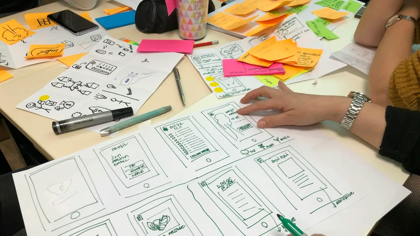 Croquis d’écrans d’application dessinés sur papier, entourés de notes adhésives