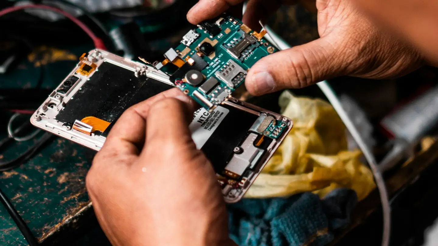Mains réparant un smartphone ouvert, carte électronique visible